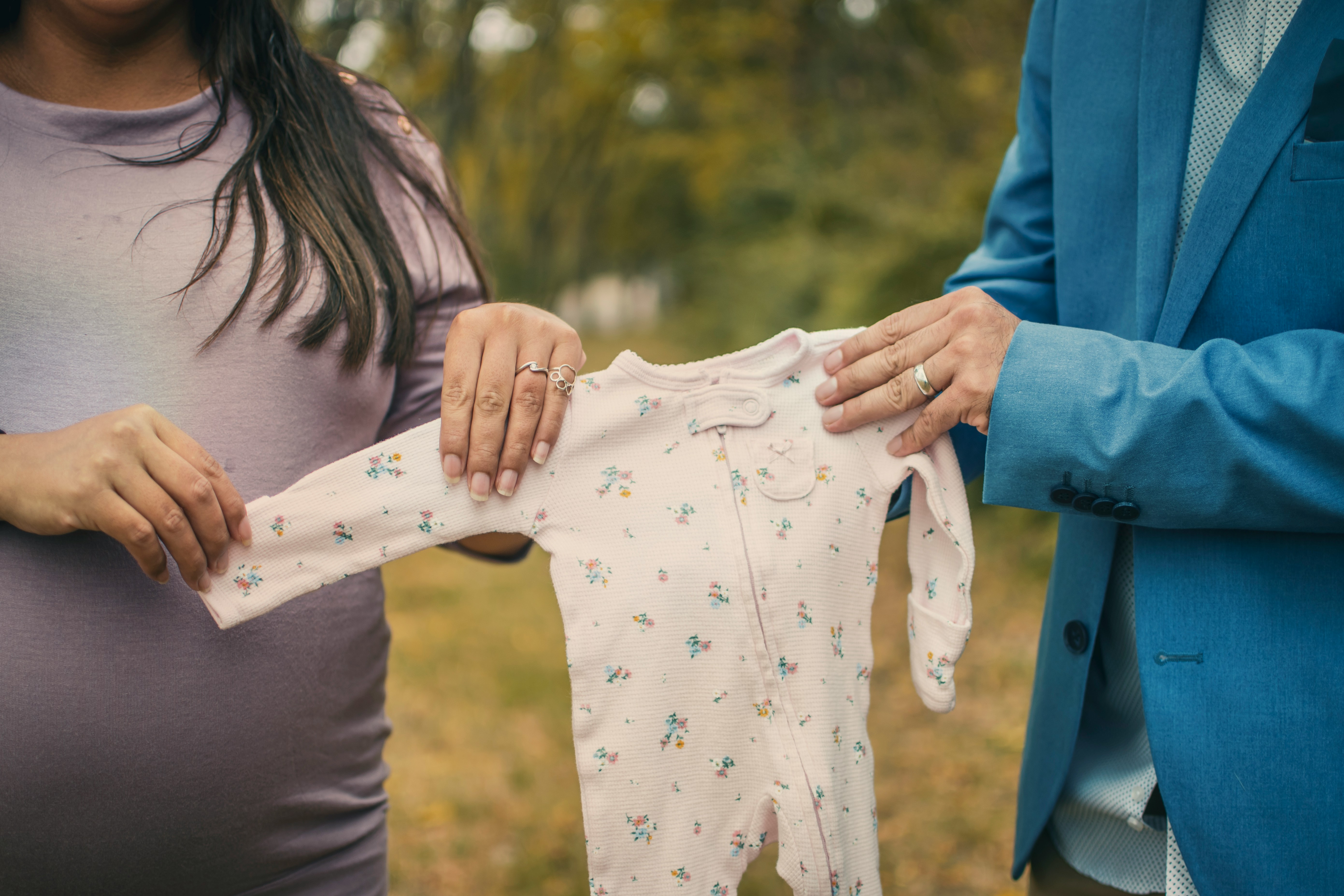 A man and pregnant woman's torsos as they hold baby pajamas in the center of the image